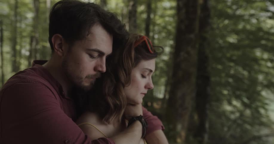 Man back hugs crying woman kissing and stroking her hair as they stand in the forest