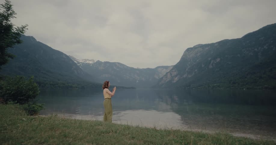 Woman walking towards a lake and stopping to take pictures of the landscape