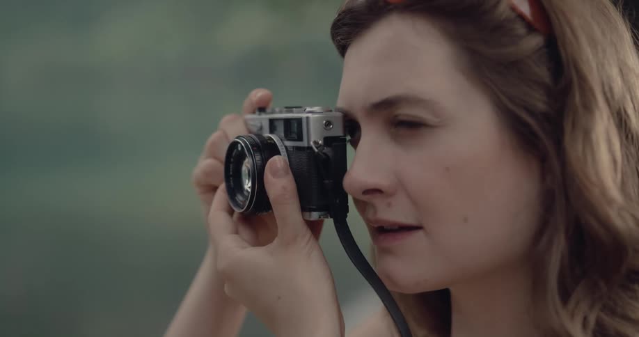 Close up of a young woman standing near a lake taking pictures with a vintage camera