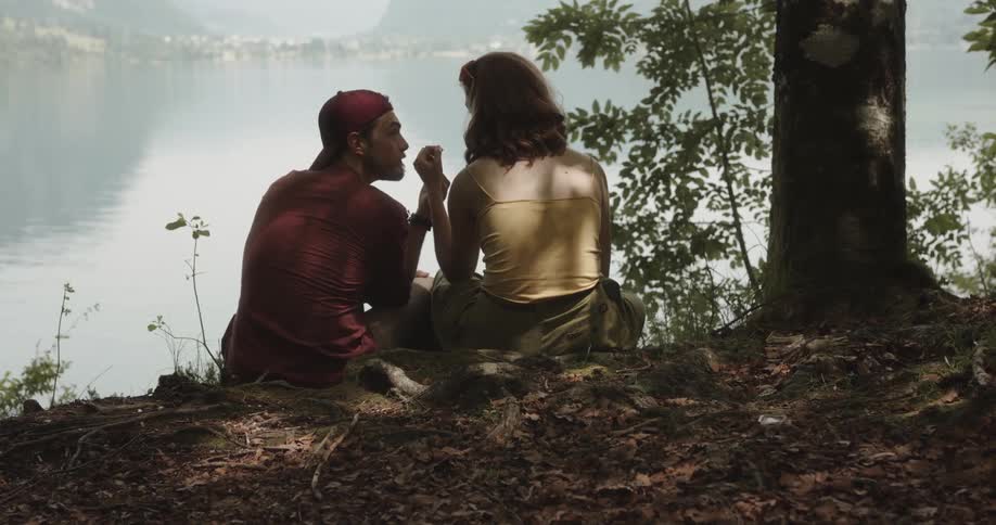 Couple sitting near a tree overlooking lake holding hands and kissing