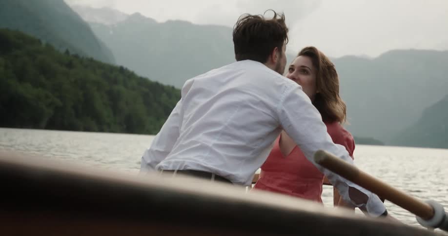 A woman plays a ukulele on a boat before the man sitting across from her approaches and kisses her