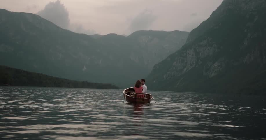 A man and woman sit on a boat and laugh and hug and kiss