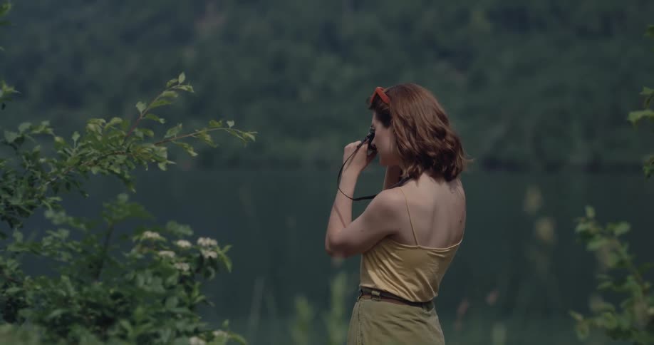 Woman standing next to a lake taking pictures of the surroundings with a digital camera