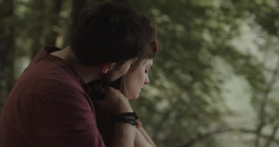 Man with red t shirt and bracelet holds sad woman and consoling her in the woods