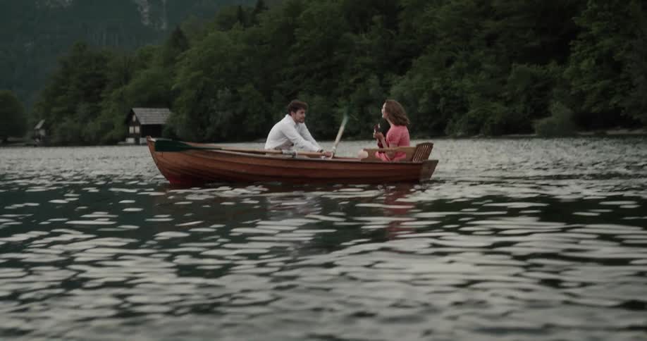 Happy young couple riding a rowboat on a lake in the mountains at morning