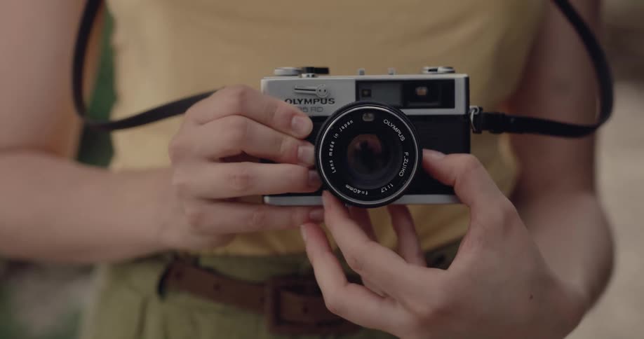 A woman uses a film camera while standing outside