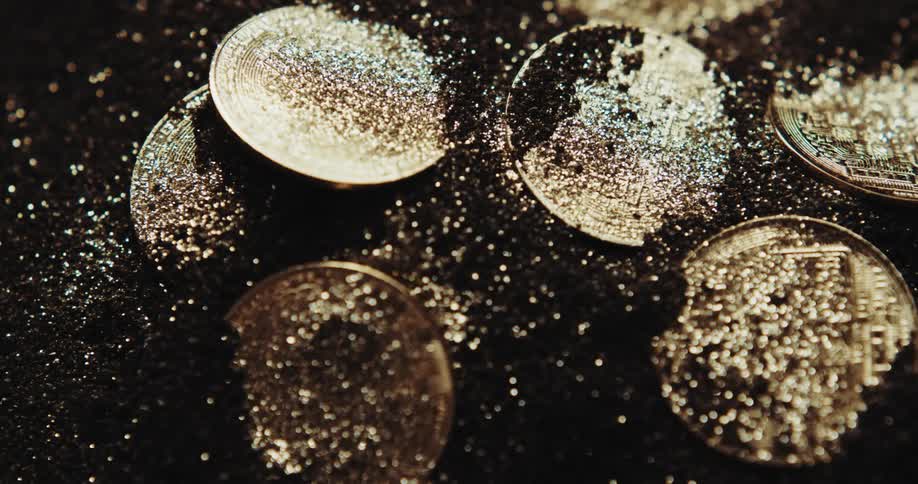 A number of coins are partially buried in a black granular powder