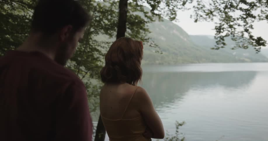 Man removes his hat in the forest and nervously approaches a woman looking out at the lake