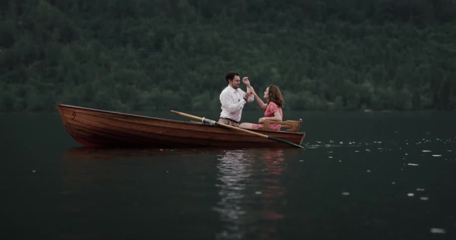Young happy couple trying to balance themselves on a rowboat kiss each other playfully