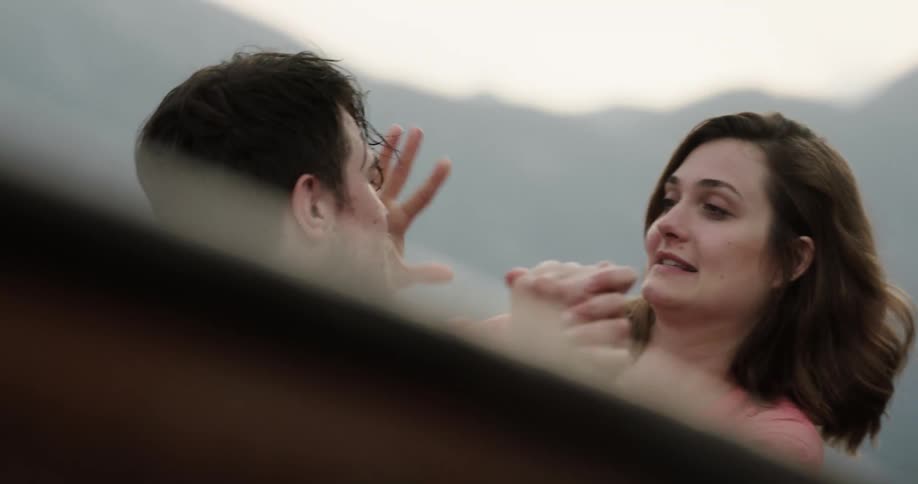 Young happy couple trying to balance themselves on a rowboat kiss each other playfully