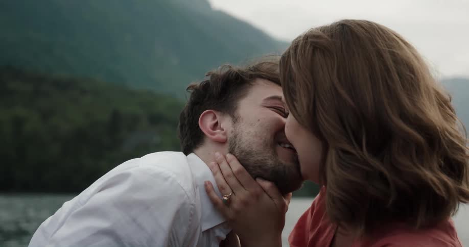 Man and woman sitting on a small boat in the middle of the lake having a date when a woman looks at her wedding ring and they kiss