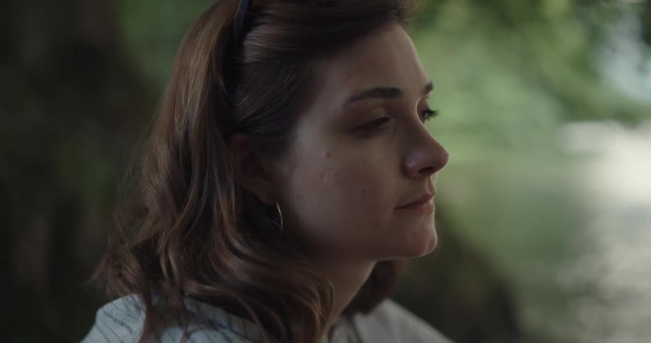 A young woman sits by a river and contemplates