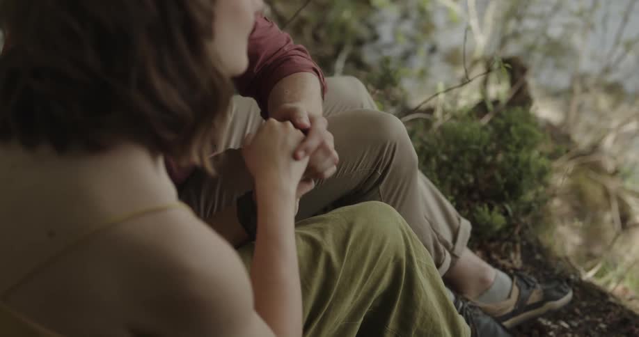 A man sitting beside a woman on the shore of a lake kisses her hand and places it on his face