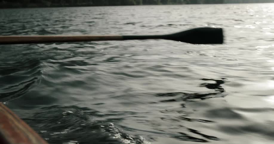 An ore is moving in and out of the water as someone rows a boat