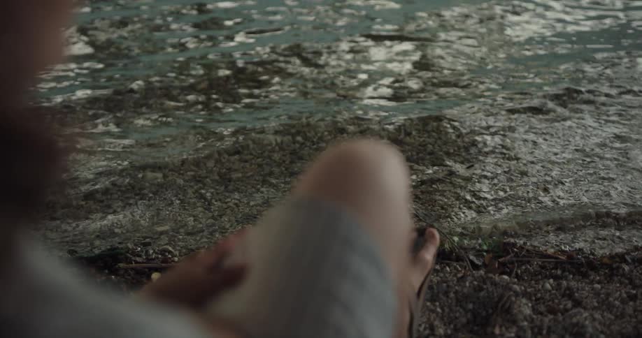A woman is sitting near the coast by a body of water