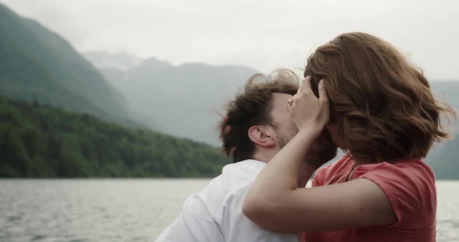 Man and woman in a wooden canoe in the middle of a lake romantically making out