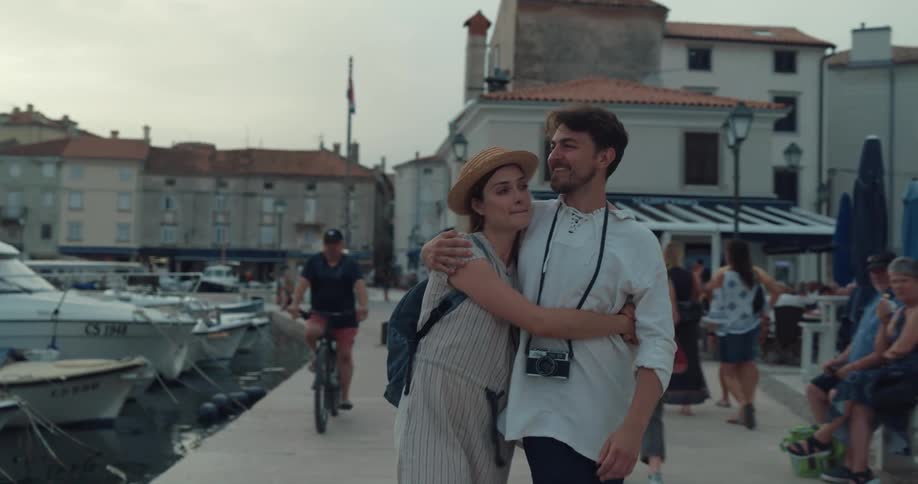 Young happy couple on vacation kiss while hugging and walking near a pier in a town