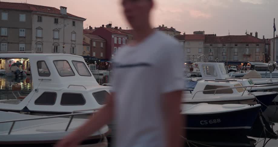 Boats sit parked at the dock in a village as a man walks by