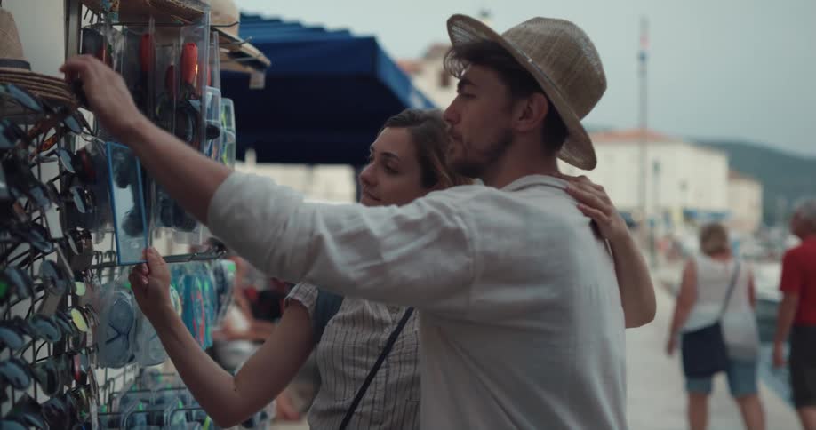 Happy tourist couple hanging out in the city trying on sunglasses and hats from a street vendor