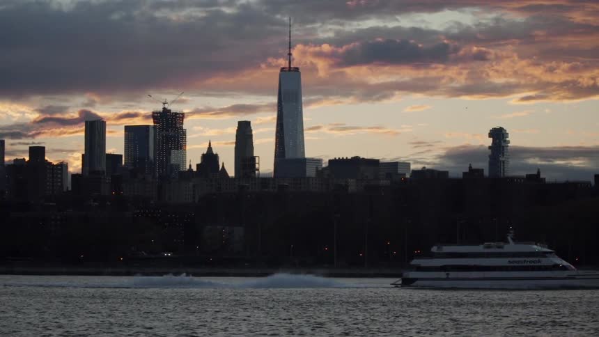 A yacht passes a city at sunset