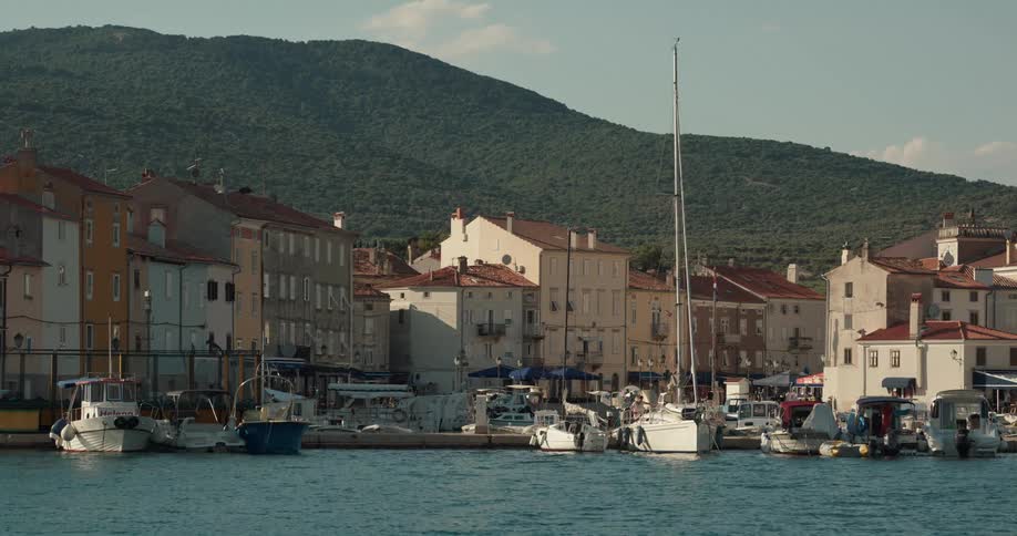Boats sit docked in the harbor next to the village as mountains sit behind the buildings