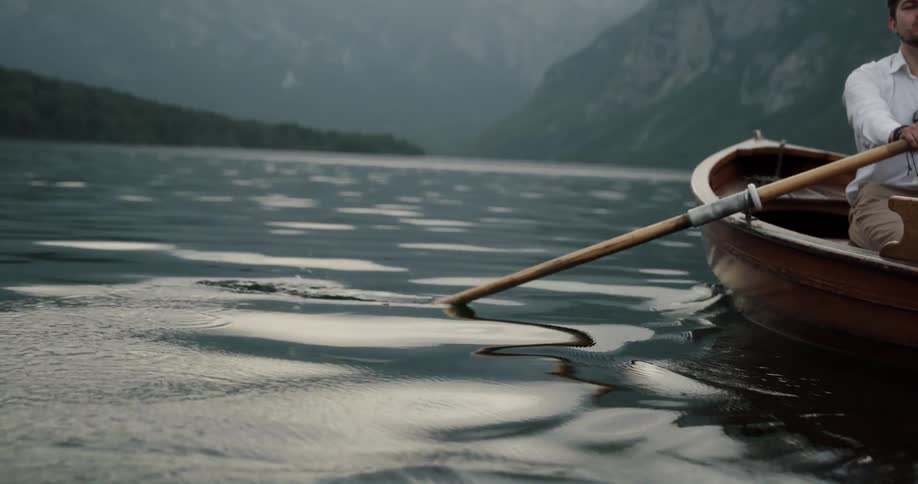 Happy young couple riding a rowboat on a lake in the mountains at morning