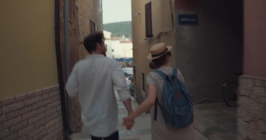 Tourist couple holding hands and happily walking down an alley of a charmful european city