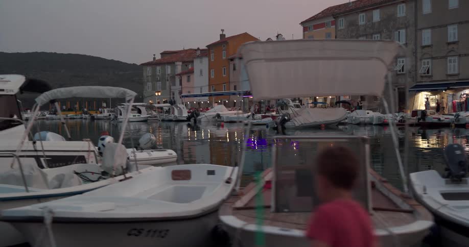 Rows of boats on a pier near the short buildings of a small coastal town at sunset