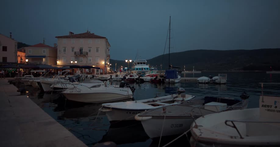 People walk around buildings near a marina where speedboats are docked