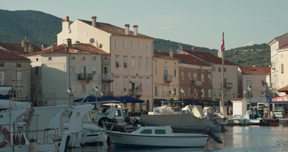Boats sit in the harbor near a town as people ride bicycles nearby