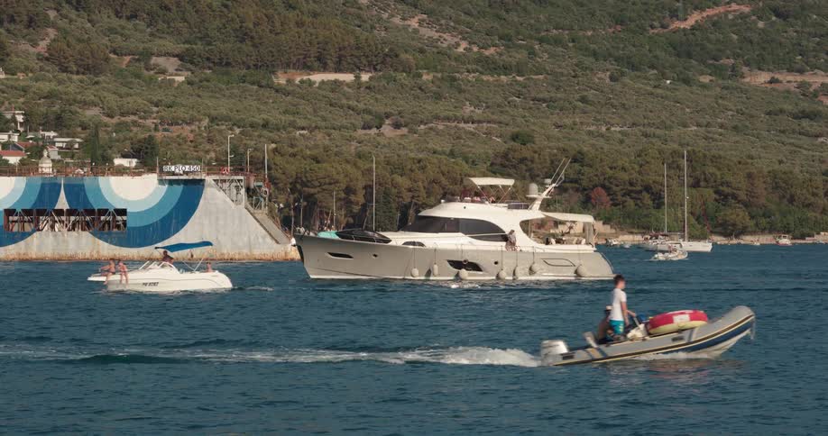 Yacht and boats move through water near shore as birds fly overhead