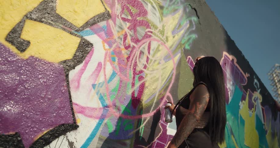 A woman uses spray paint to draw on the facade of a building during the day
