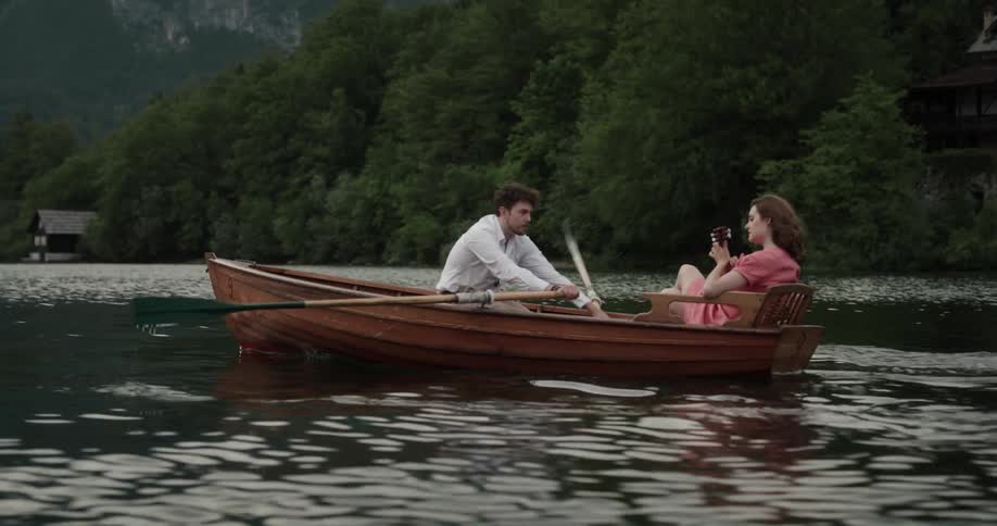 Happy young couple riding a rowboat on a lake in the mountains at morning