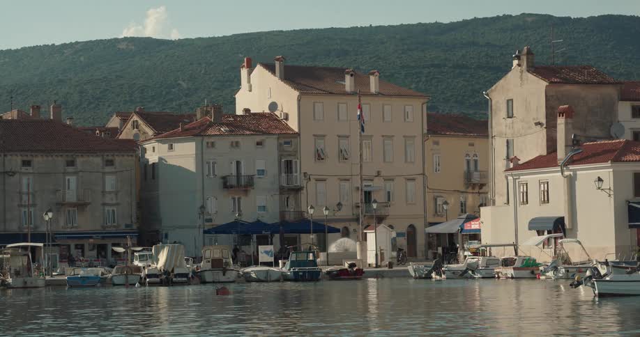 View of coastal town with buildings overlooking harbor in which boats lying at anchor