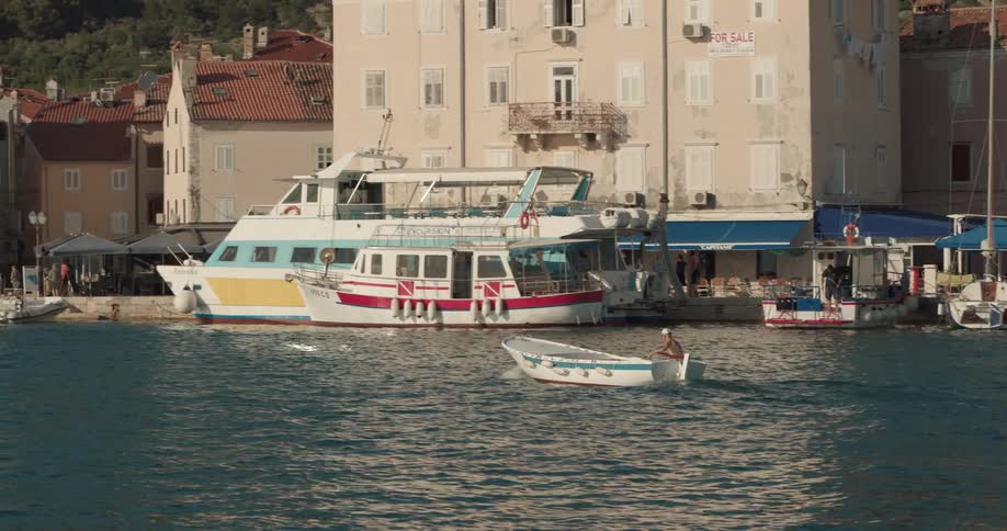 A shirtless man rides a boat along the coast of a city during the day