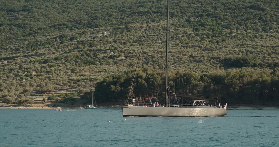People traveling on a sail boat near the coast close to the mountain