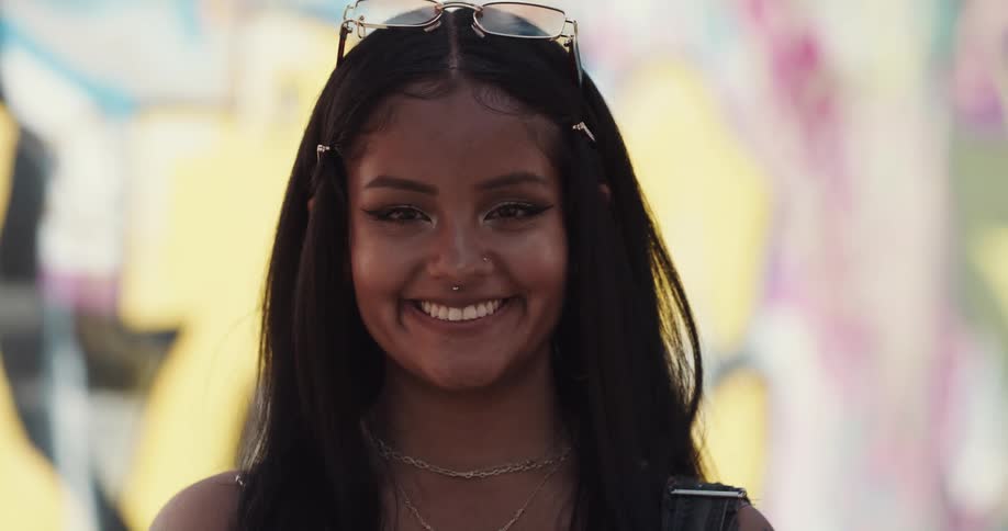 A young woman standing outdoors while posing for the camera looks up and smiles