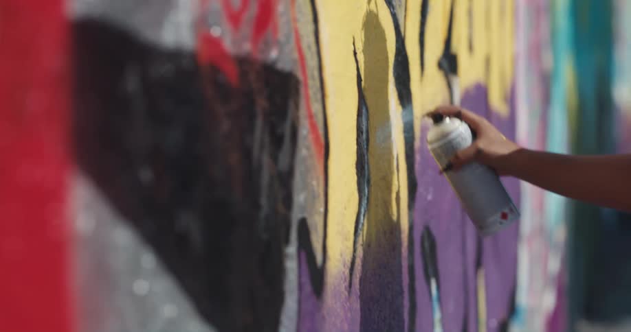 Young woman wearing a black face mask test spray cans before using them to paint graffiti on a wall