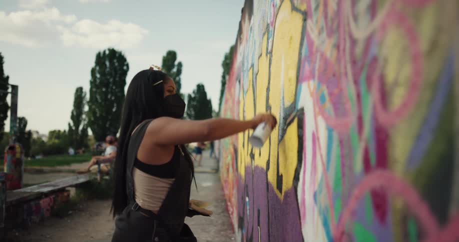 A woman is painting graffiti on a wall in a city
