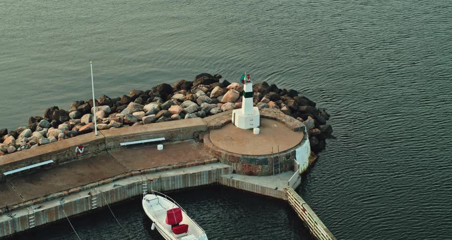 Aerial view of a lighthouse at the end of a pier next to the ocean