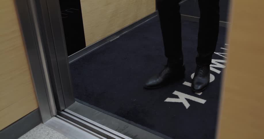 Elevator door opens and man with black leather shoes and pants gets out of it