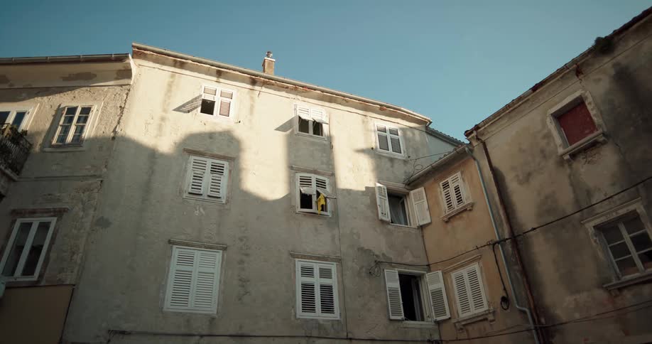 Windows are shuttered or wide opened in a large old stone building