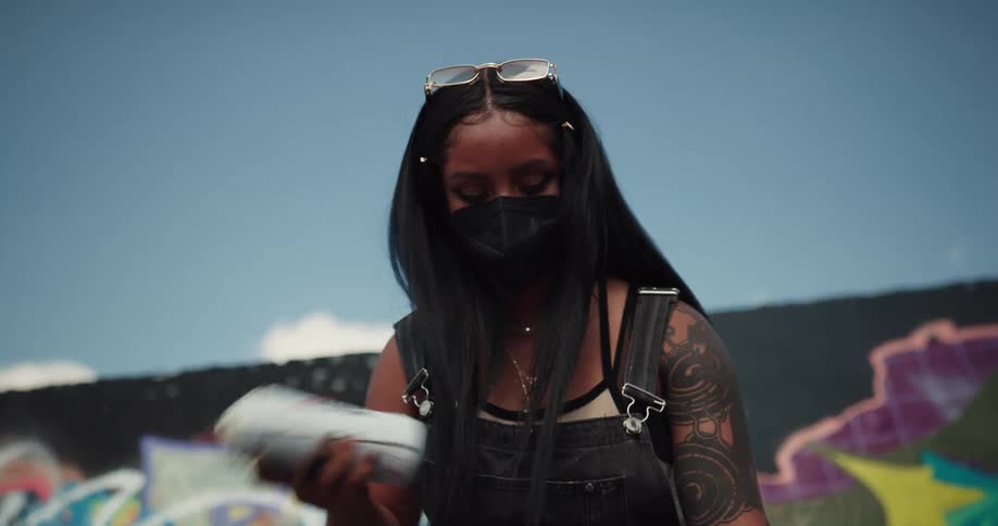 Black woman wearing a face mask choosing which spray paint can she is going to pick to do graffiti in the wall