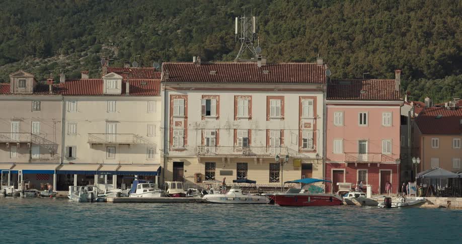 Tourists walk along the shore past shops and docked boats