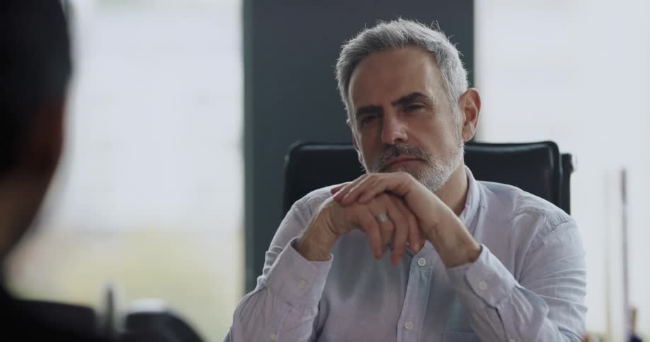 A man sits with hands folded nodding and listening intently during a meeting