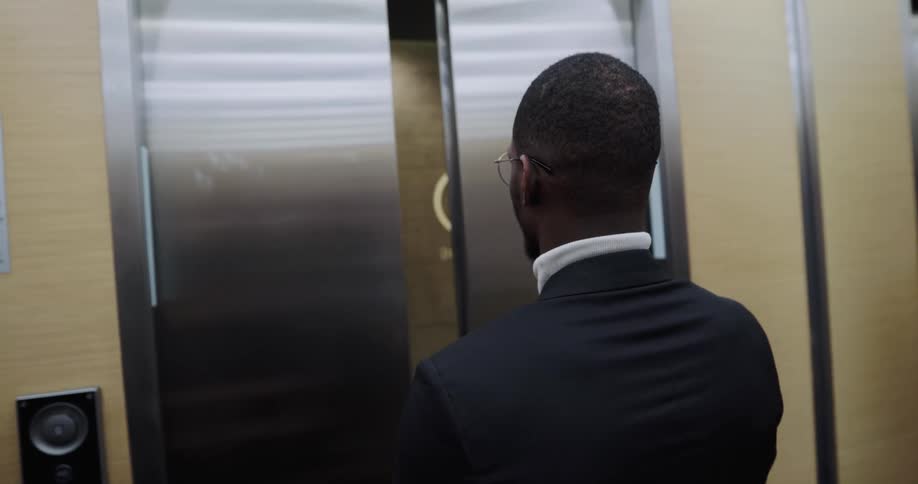 Man wearing business suit exits elevator onto office floor