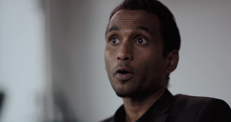 Businessman with black shirt and blazer jacket talks to person in the office