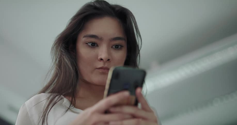 A young woman smiles and nods her head while using her smartphone indoors