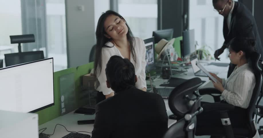 A woman sits on her colleagues desk while chatting in the office