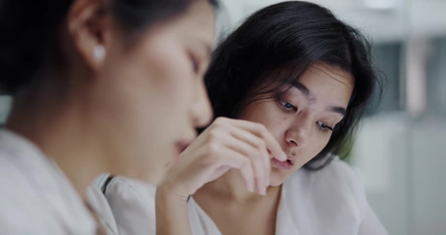 Woman sitting at a desk in a busy office talks to a coworker